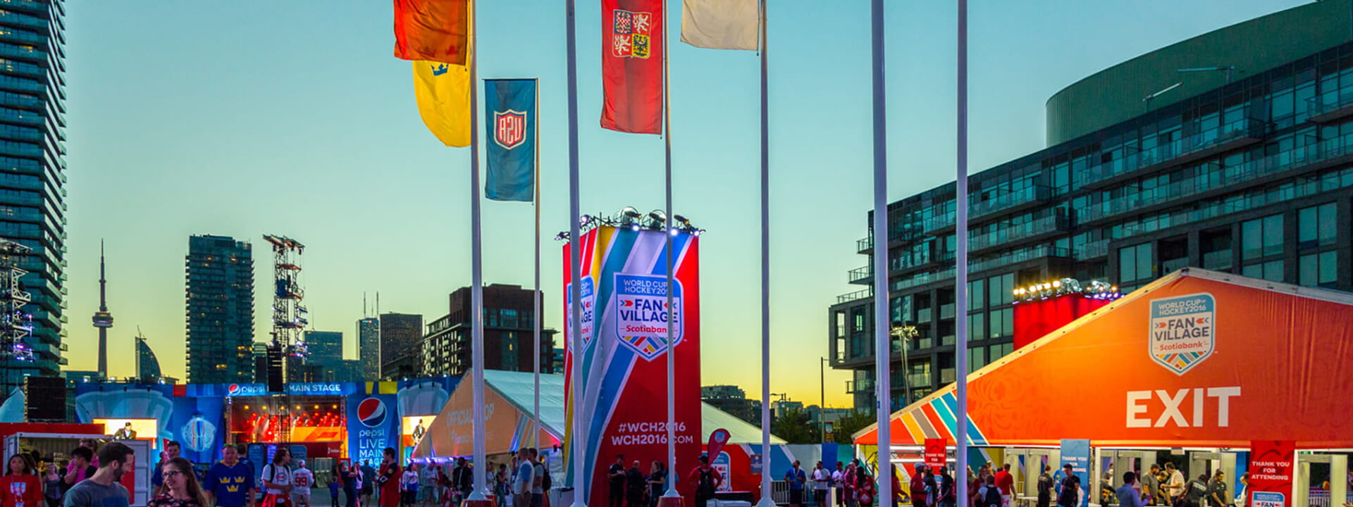 A bustling outdoor World Cup Hockey 2016 Fan Village in Toronto, featuring event tents, flags, and the CN Tower against a twilight sky.