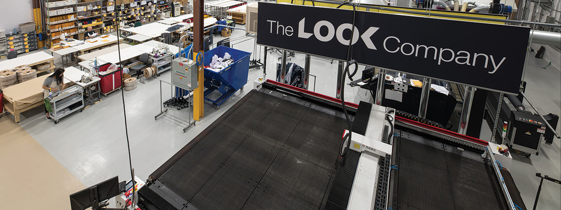The LOOK Company's production floor with an automated fabric cutting machine and employees at workstations.