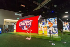 "An MLB All-Star Fanfest exhibit features a large red display with the event logo, surrounding baseball player images, and a green turf floor."
