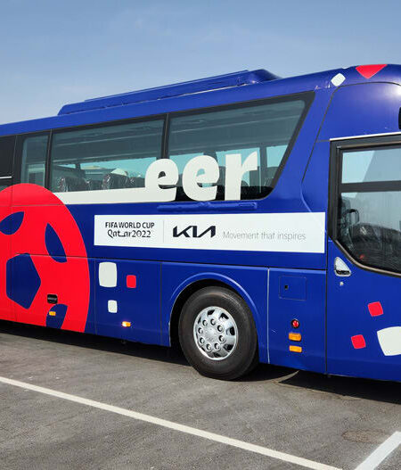 A blue and red FIFA World Cup Qatar 2022 bus with ""Cheer"" text, a football design, and a USA flag on its side.