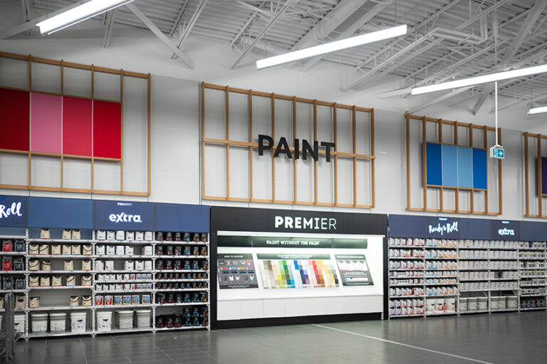 "A bright, organized paint department in a store, showing shelves of paint cans, color displays, and a large ""PAINT"" sign on the wall."
