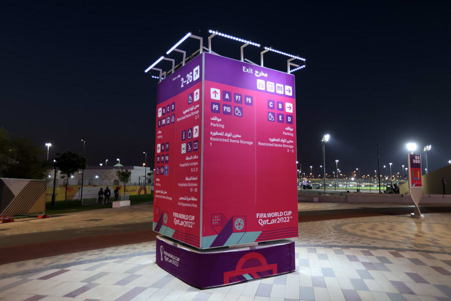 A large illuminated FIFA World Cup Qatar 2022 directional sign with Arabic and English text stands prominently at night.