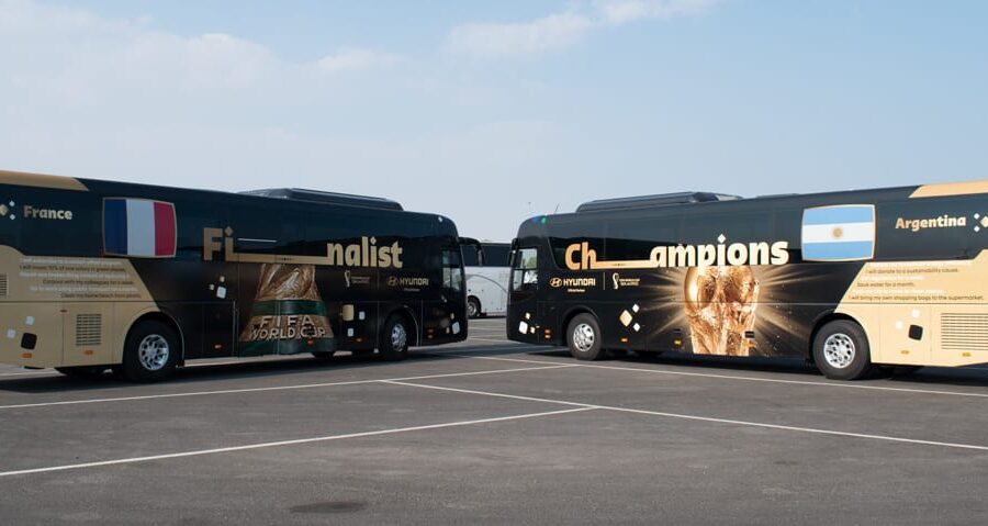 "Two FIFA World Cup-themed buses, one for ""France Finalist"" and the other for ""Argentina Champions,"" are parked side-by-side in a lot."
