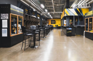 "A modern black and yellow Tiger-Cats alumni hall featuring sports memorabilia displays, a long row of high-top tables, and open locker cubbies."