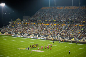 A high-angle view of a night football game with players on the field and spectators in a brightly lit stadium.