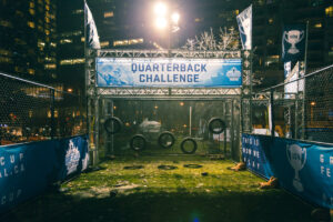 "An illuminated outdoor football ""Quarterback Challenge"" game featuring tire targets and scattered footballs, set up at night during the Grey Cup Festival."