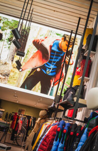 "A modern clothing store interior with a large billboard of a man in outdoor wear, flanked by racks of colorful jackets and display shelves."