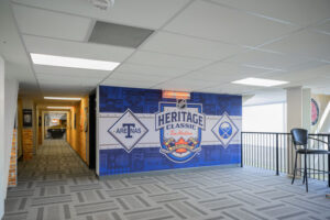 "A modern commercial interior features a large blue wall mural promoting the NHL Heritage Classic, flanked by Buffalo Sabres and Arenas logos, alongside a long hallway."