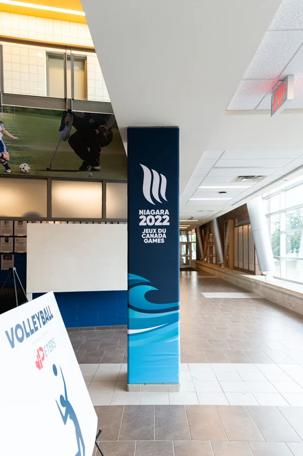 A hallway in a sports facility featuring a prominent Niagara 2022 Canada Games banner and sports-themed wall graphics.