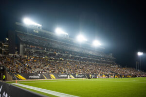 "A brightly lit football stadium at night, with green turf and thousands of spectators filling the stands."