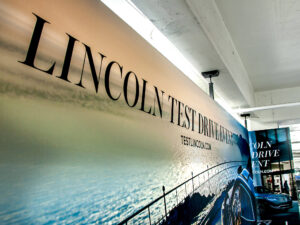 "A large banner advertises a ""Lincoln Test Drive Event"" with a blue Lincoln car and a scenic water background."