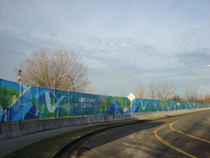 "A long blue and green banner featuring ""Vancouver 2010"" and the Olympic rings stretches alongside a curving road."