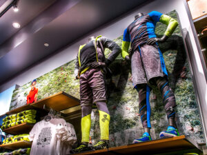 "Two mannequins display colorful Under Armour athletic wear in a retail store, set against a large background image of a grassy field."