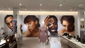 "Interior of a modern fashion store featuring oversized wall portraits of diverse models, a mannequin in a patterned dress, and multiple shoe displays."