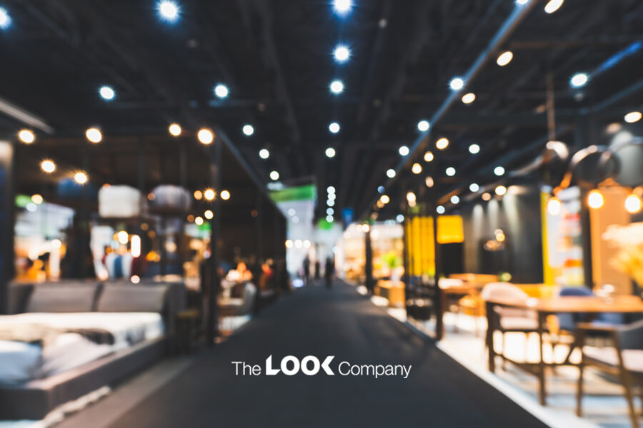 Blurred interior of a modern furniture showroom with bright lights, various displays, and ""The LOOK Company"" logo on a dark floor.