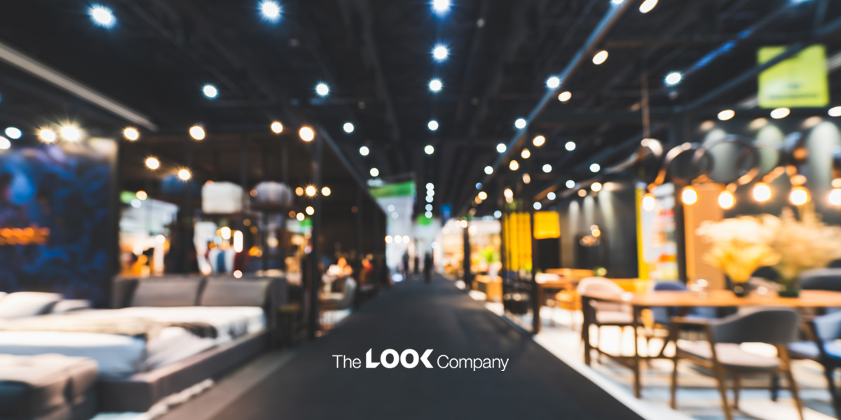 Blurred interior of a modern furniture showroom with bright lights, various displays, and ""The LOOK Company"" logo on a dark floor.