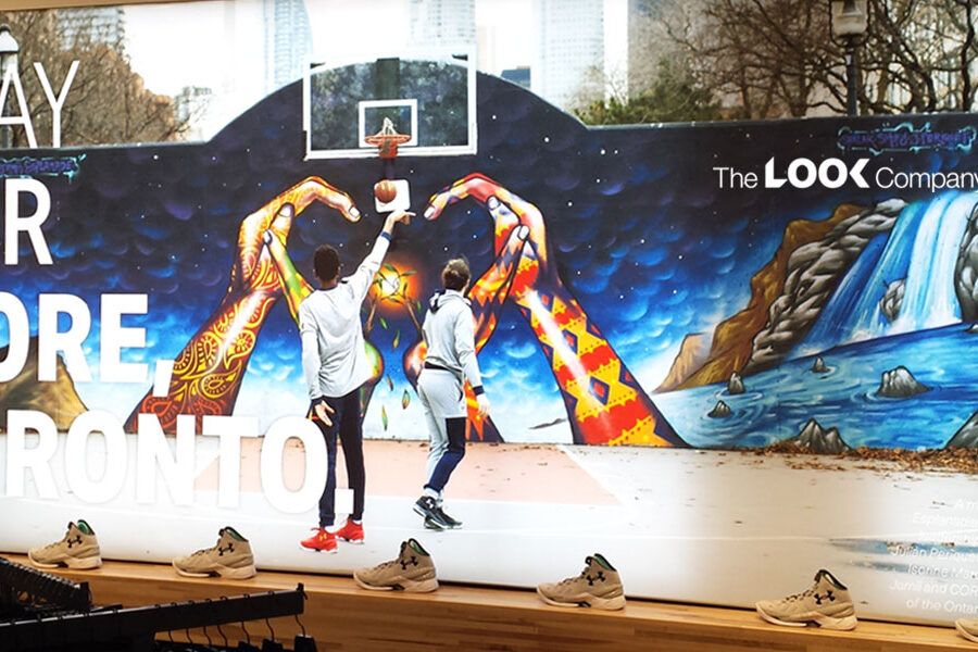 A vibrant mural displays ""PLAY FOR MORE TORONTO"" with two basketball players forming a heart against a starry sky and waterfalls, surrounded by Under Armour shoes on a ledge.