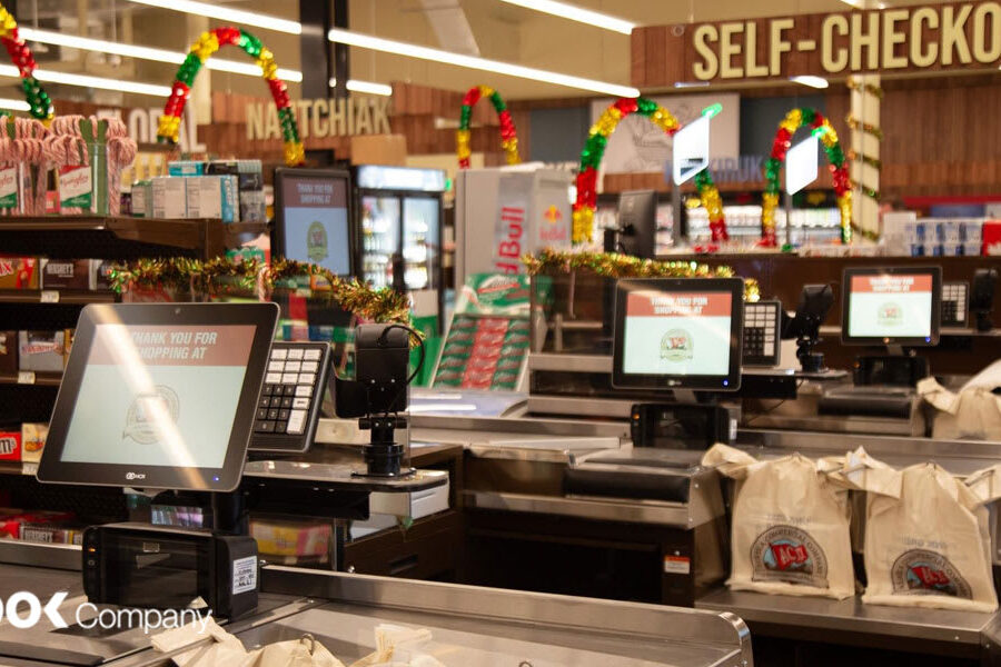 Festively decorated self-checkout stations in a grocery store, with candy and snack displays visible nearby.