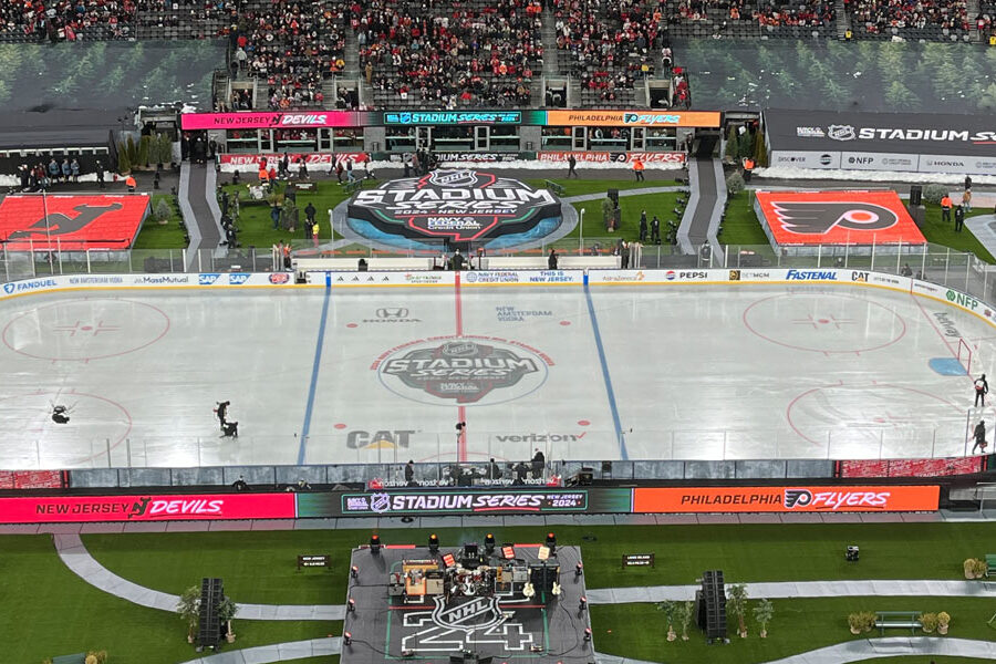 An outdoor hockey rink in a stadium, set up for the NHL Stadium Series 2024 between the New Jersey Devils and Philadelphia Flyers, with a concert stage visible.