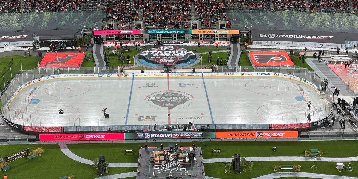 An outdoor hockey rink in a stadium, set up for the NHL Stadium Series 2024 between the New Jersey Devils and Philadelphia Flyers, with a concert stage visible.