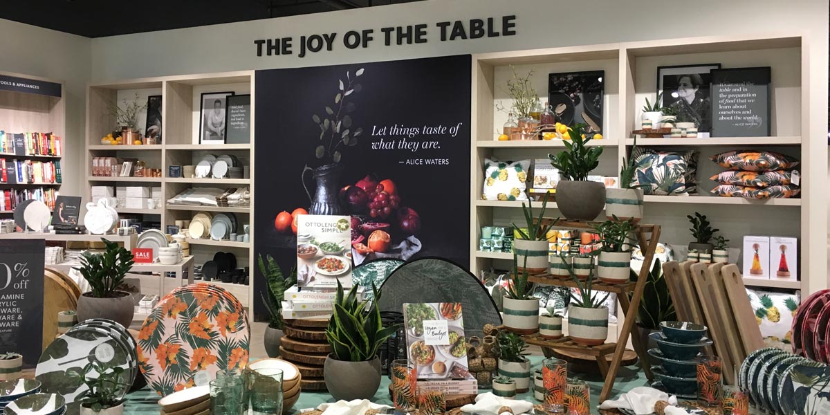 A store display of kitchenware, cookbooks, and home decor items under a sign reading ""THE JOY OF THE TABLE.""
