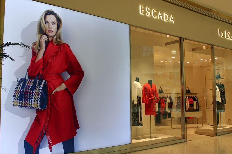 Escada store exterior featuring a large advertising poster of a model in a red coat and a patterned bag, next to its glass display window.