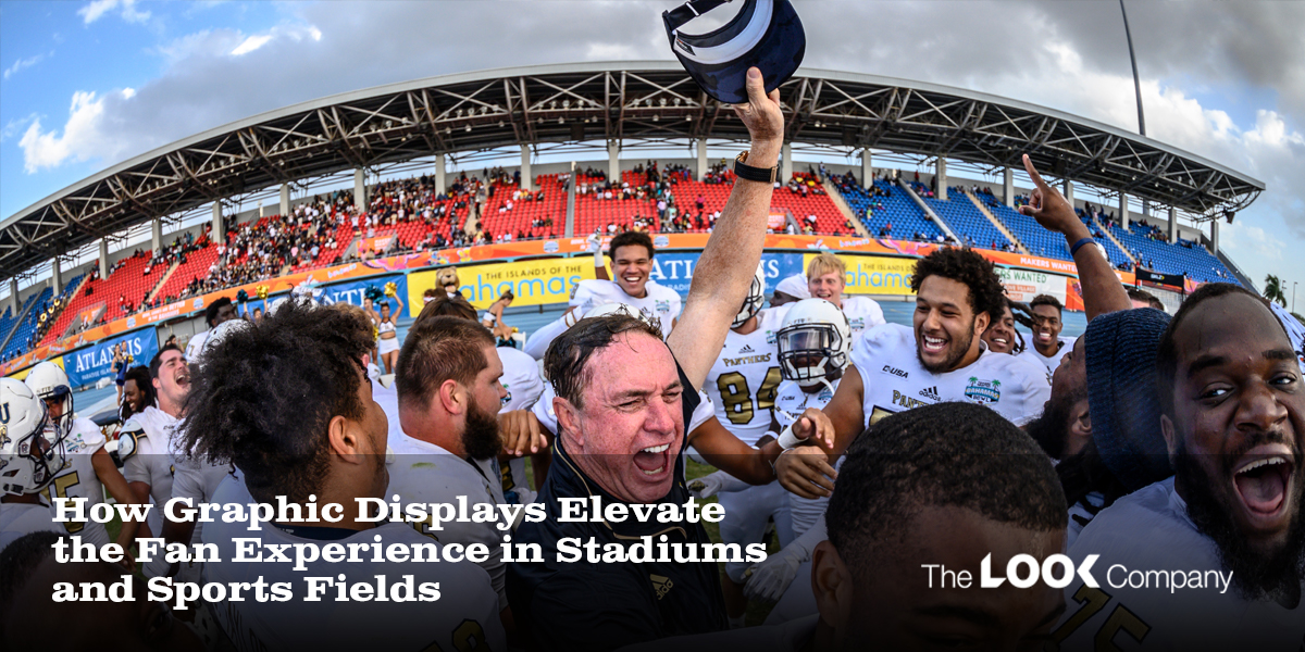 Excited football players and their coach celebrate on a field with a stadium full of fans and large graphic displays.