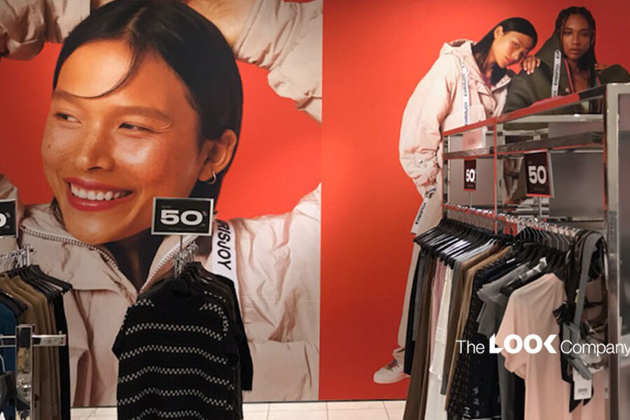 A retail store display featuring large red wall graphics of models, ""50"" sale signs, and racks of clothing.