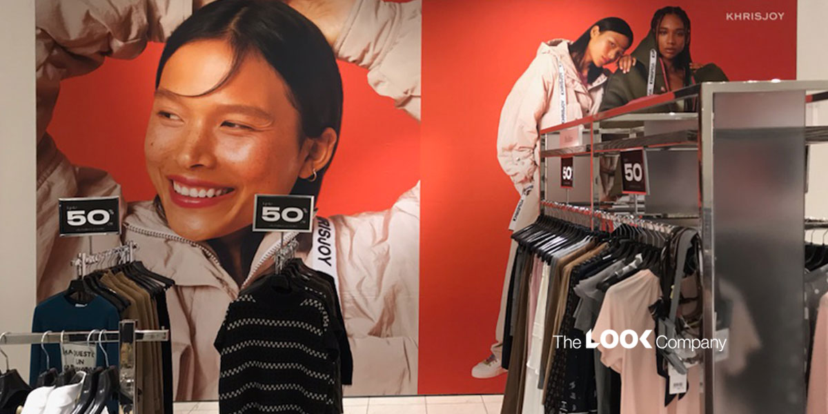 A retail store display featuring large red wall graphics of models, ""50"" sale signs, and racks of clothing.