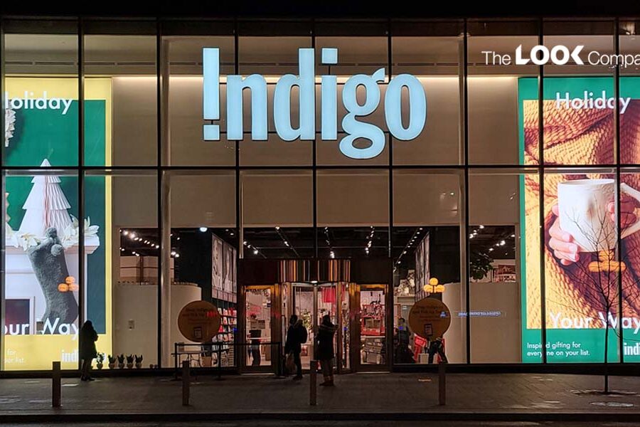 Illuminated Indigo store facade at night with festive ""Holiday Your Way"" window displays.