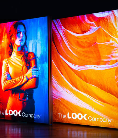 Two illuminated vertical displays from The LOOK Company show a woman in colorful light and an abstract orange pattern.