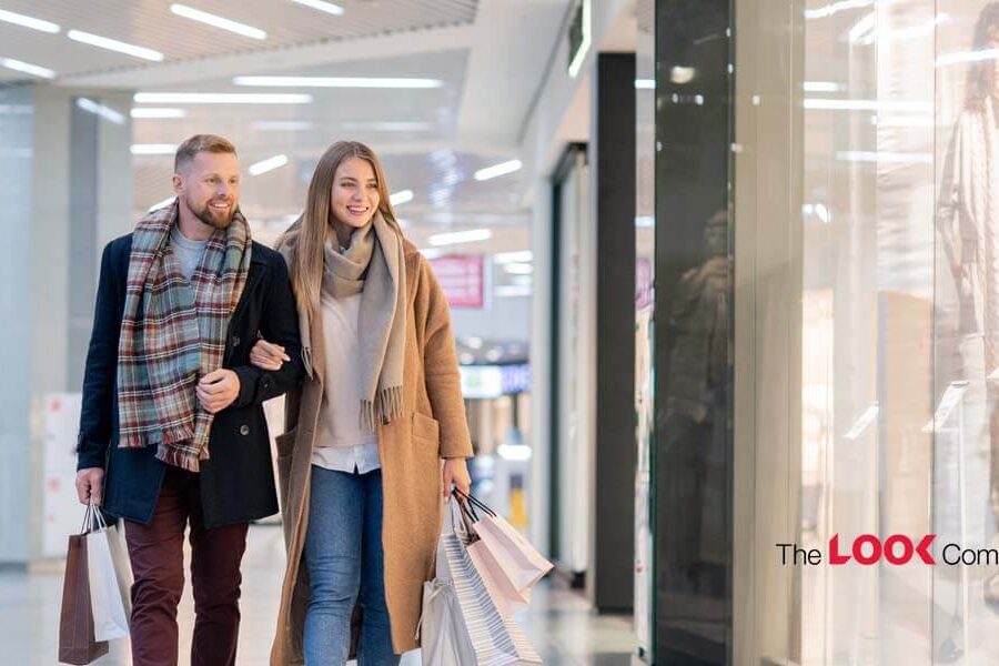 A smiling couple walks arm-in-arm through a shopping mall, carrying shopping bags.