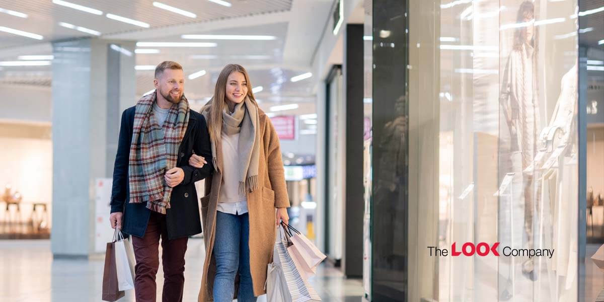 A smiling couple walks arm-in-arm through a shopping mall, carrying shopping bags.