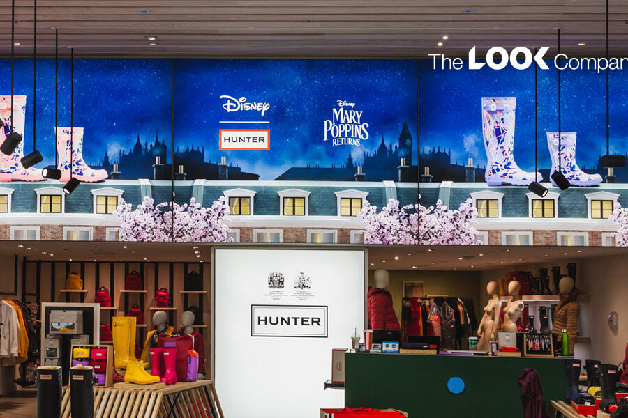 A vibrant Hunter retail store interior features a large digital display promoting a Disney Mary Poppins Returns collaboration with stylized rain boots, above colorful clothing and footwear merchandise.