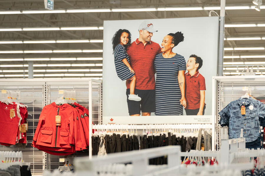 A large poster of a smiling, diverse family in coordinating outfits is displayed in a retail store surrounded by clothing racks.