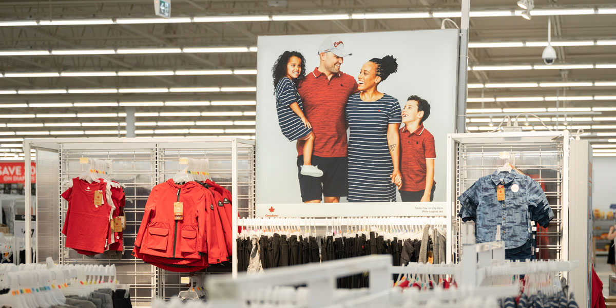 A large poster of a smiling, diverse family in coordinating outfits is displayed in a retail store surrounded by clothing racks.