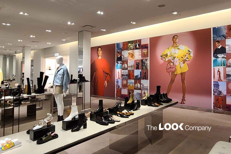 Interior of a fashion retail store with shoes and clothing on display, featuring large wall graphics of models and ""The LOOK Company"" logo.