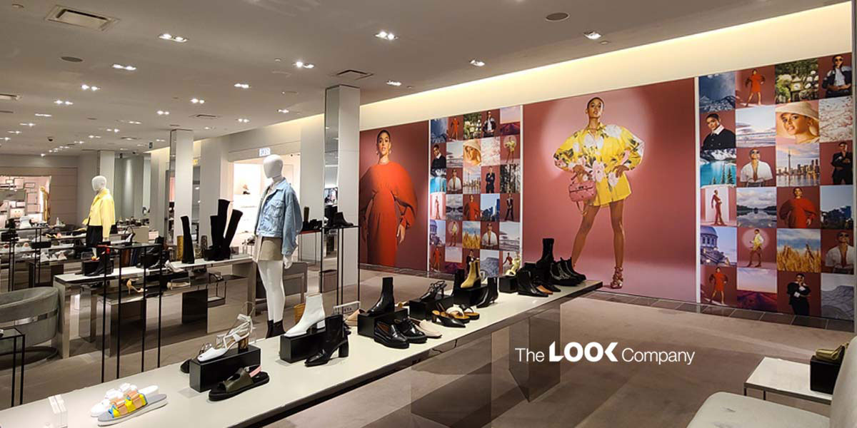 Interior of a fashion retail store with shoes and clothing on display, featuring large wall graphics of models and ""The LOOK Company"" logo.