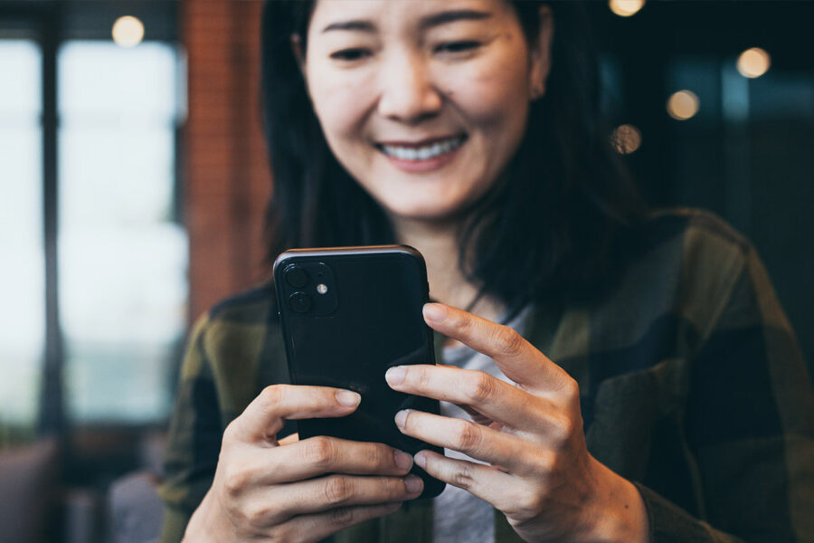 A smiling Asian woman holds and uses a smartphone.