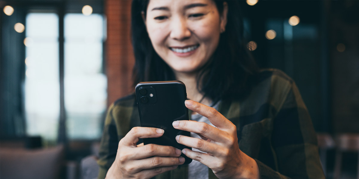 A smiling Asian woman holds and uses a smartphone.