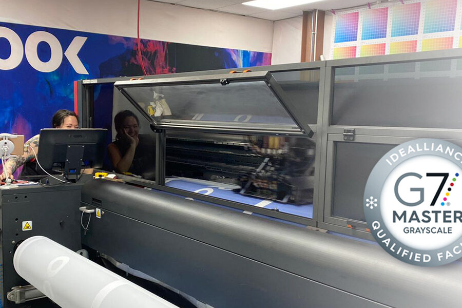 An employee operates a large industrial printer in a G7 Master Grayscale Qualified Facility.