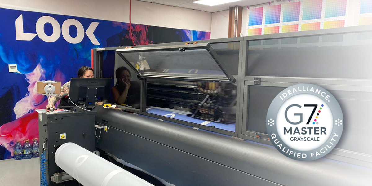 An employee operates a large industrial printer in a G7 Master Grayscale Qualified Facility.