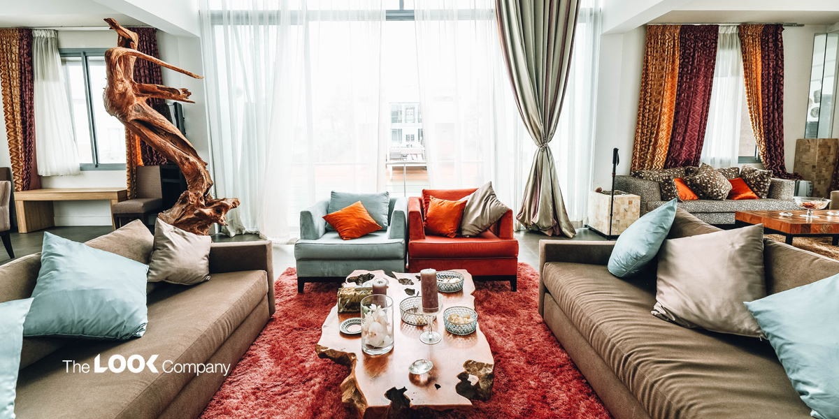 A brightly lit, modern living room features a large driftwood sculpture, colorful sofas, a live-edge coffee table, and a vibrant red shag rug.