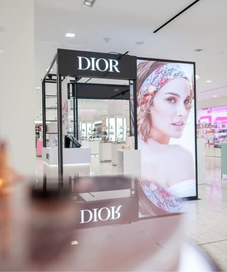 A bright, modern Dior cosmetics display features a large advertisement of a woman wearing a headscarf inside a retail store.