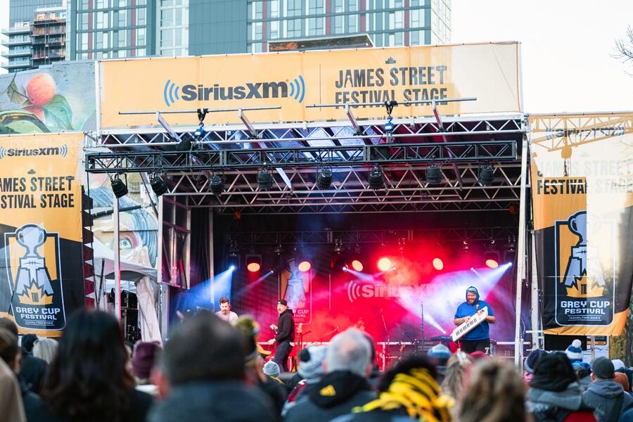 A band performs on the brightly lit SiriusXM James Street Festival Stage for a crowd at the Grey Cup Festival 2023 in Hamilton.