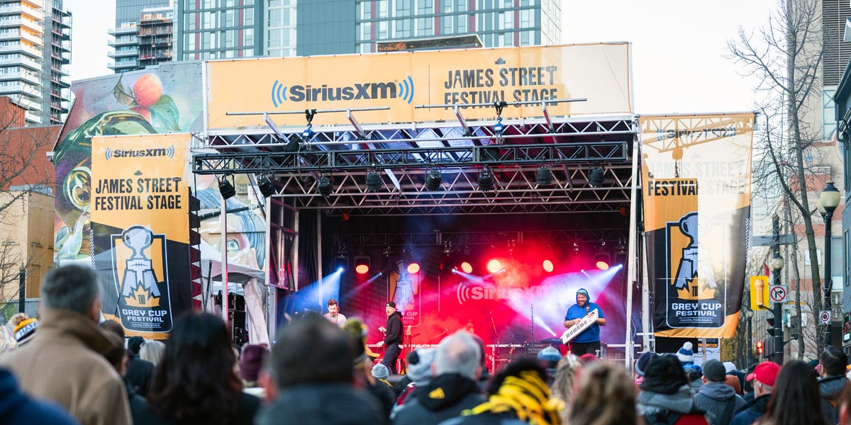 A band performs on the brightly lit SiriusXM James Street Festival Stage for a crowd at the Grey Cup Festival 2023 in Hamilton.