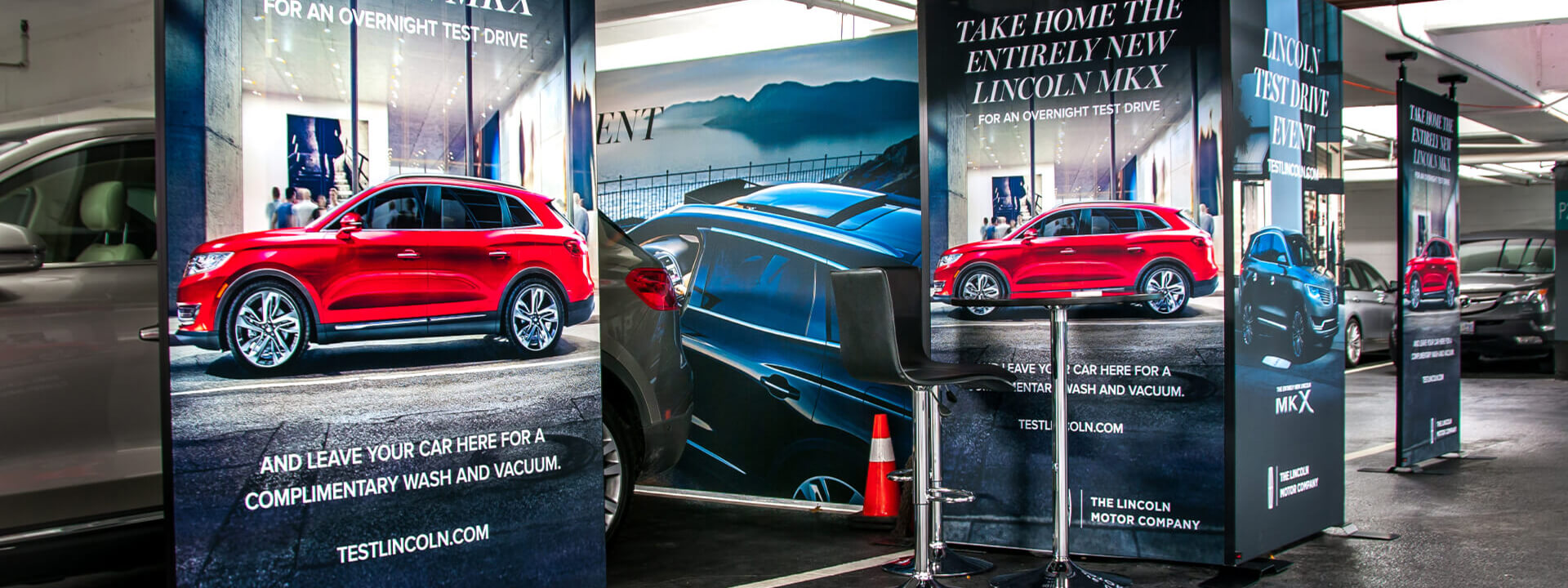 Promotional banners for a Lincoln MKX overnight test drive event set up in an indoor parking garage.