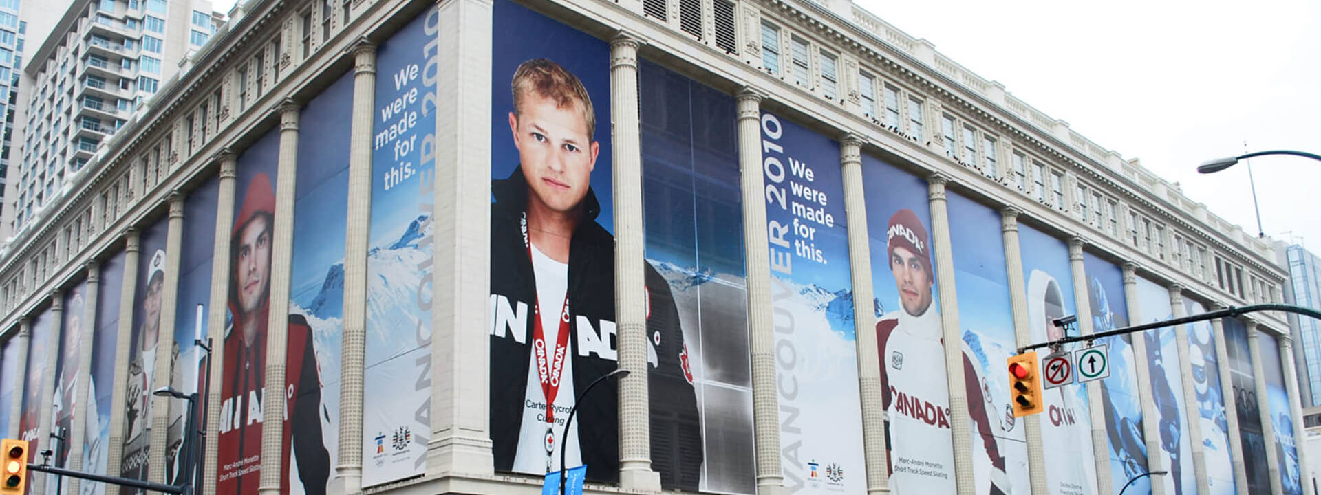 A building is covered with large banners for the Vancouver 2010 Olympics, showcasing Canadian athletes and the slogan 'We were made for this.'