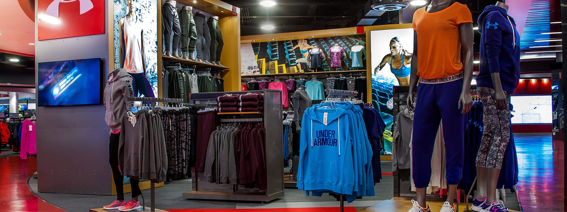 Interior of a brightly lit Under Armour store, displaying athletic apparel on mannequins and clothing racks.