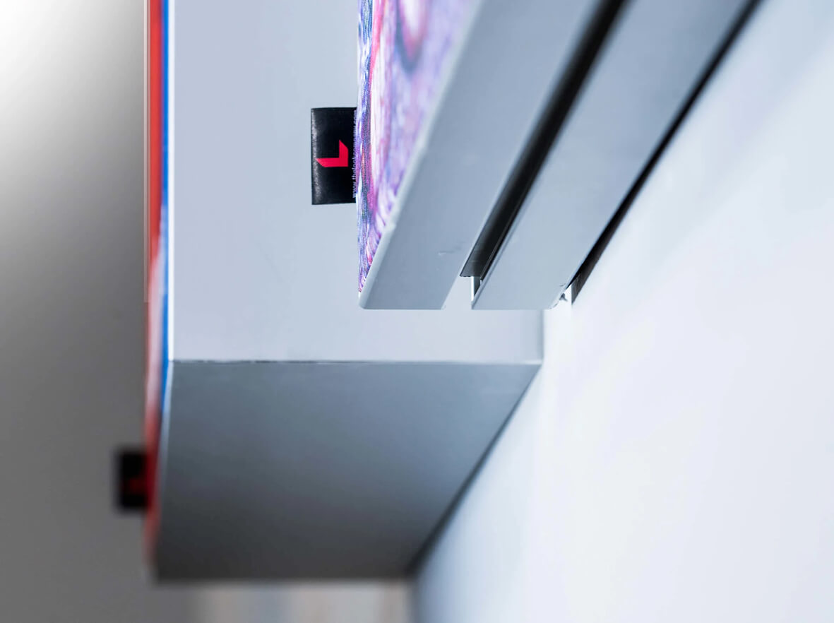 Close-up of a colorful print with a black pull tab featuring a red 'L' logo, mounted in a gray wall display track.
